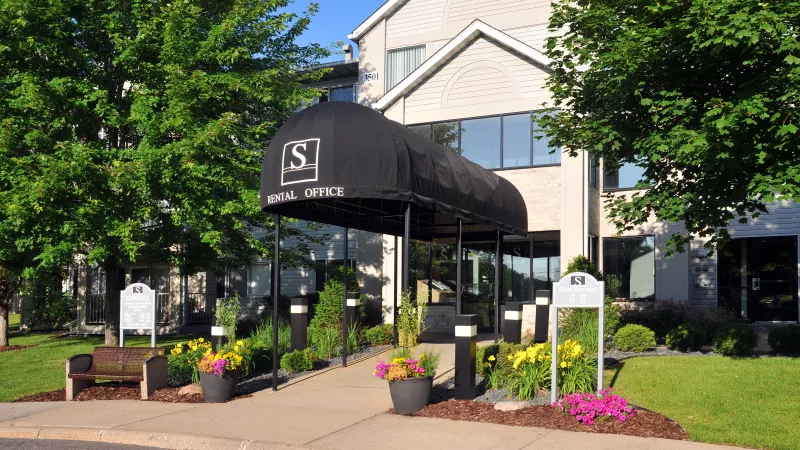 Building entrance with black "South Shore" awning, surrounded by vibrant green trees and colorful flowers in pots.