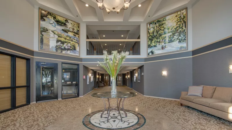 Elegant hotel lobby featuring a chandelier, two large wall murals, a central glass table with flowers, and a beige sofa.