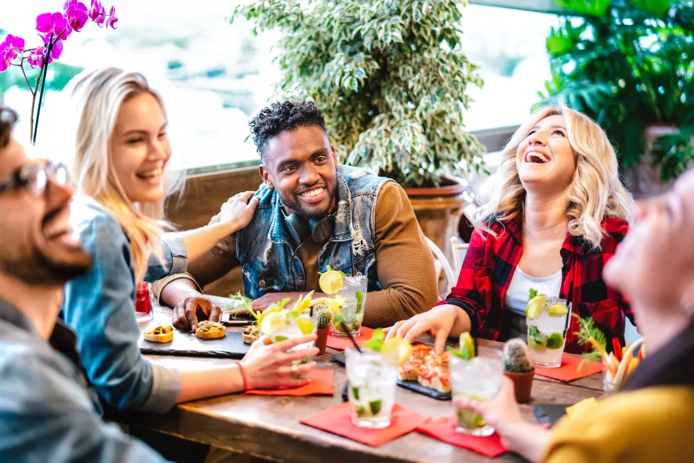 Smiling friends share laughs and drinks at a vibrant restaurant or bar.